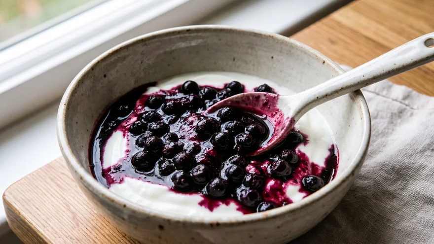 Dark purple aronia berry compote over plain yogurt in a ceramic bowl